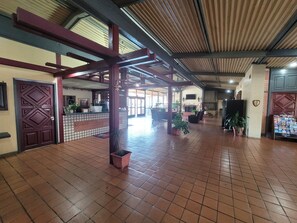 A spacious lobby with a tiled floor, a reception desk, and several potted plants.