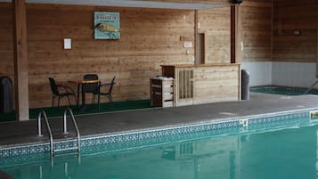 Área de piscina com paredes de madeira, uma espreguiçadeira, uma mesa pequena e uma placa indicando uma sauna.