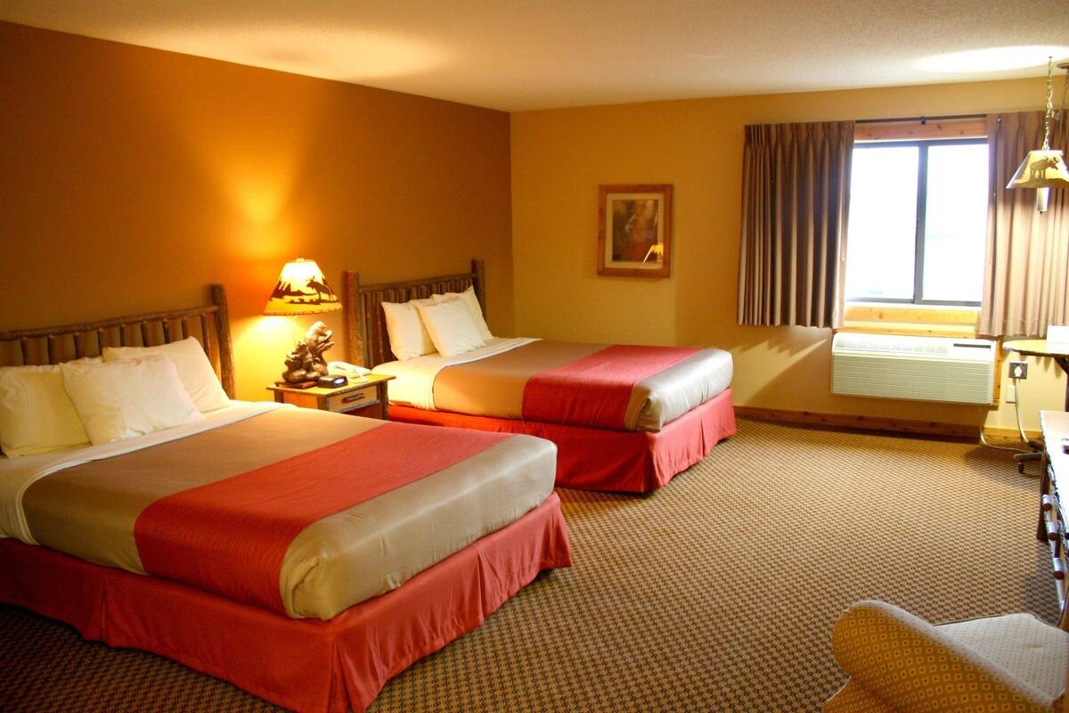 A hotel room with two beds, a desk, a chair, and a window with curtains.
