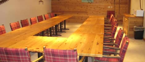 A long wooden table with plaid chairs, a television on the wall, and a sign that reads "The Lodge."