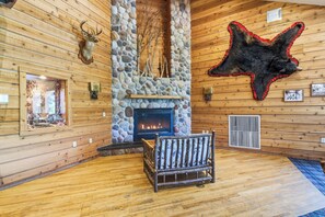 A log cabin interior with a stone fireplace, a mounted deer head, a bear hide, and a rustic wooden bench. - The Lodge at Crooked Lake (Siren)