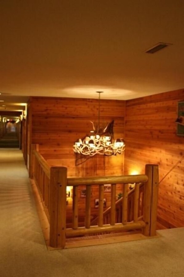 A wooden interior with a staircase, a chandelier, and a wooden railing.