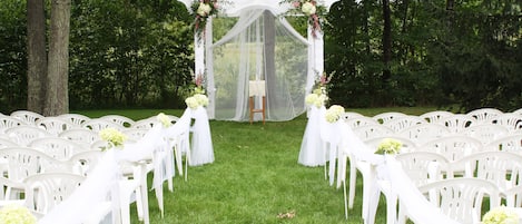 A wedding aisle with white chairs and a canopy.