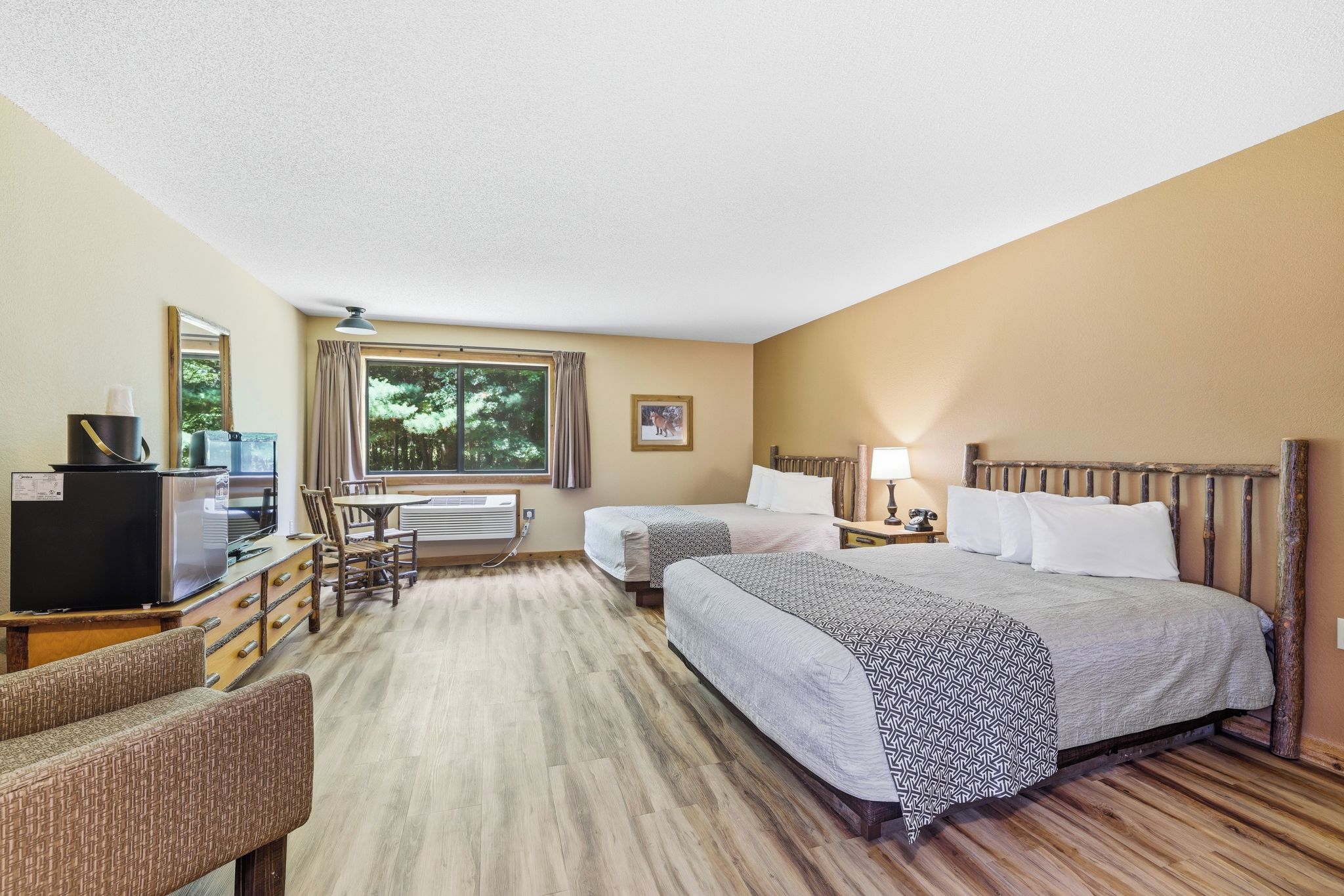 Quarto de hotel com duas camas, uma mesa de trabalho com televisão e janela com cortinas.