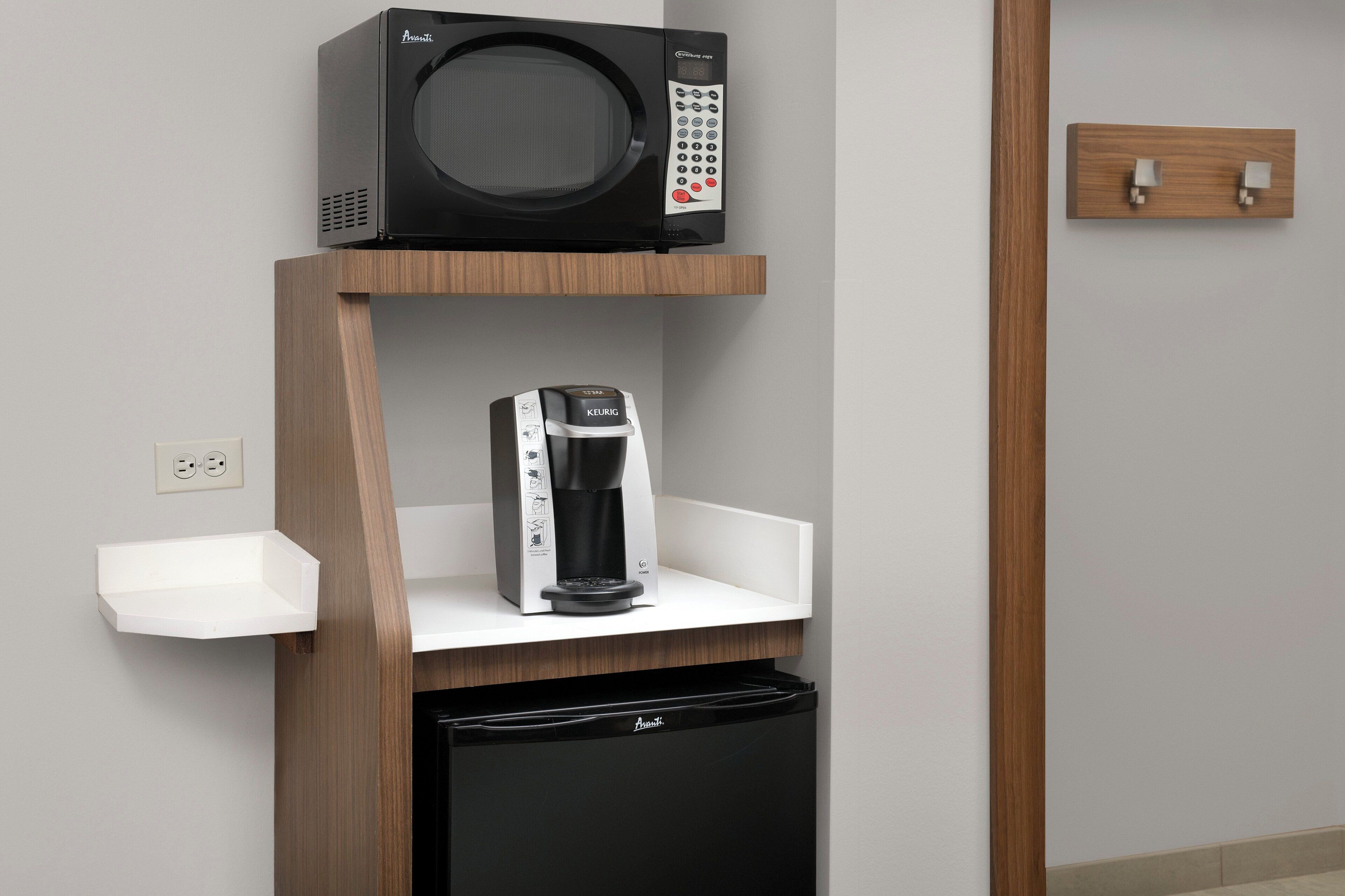 A kitchenette with a microwave, coffee maker, and a black refrigerator.