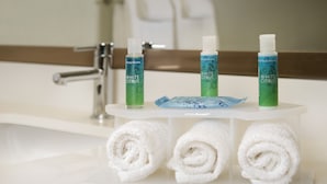 A bathroom with a white sink, three bottles of White Citrus body wash, and three rolled white towels on a white shelf.