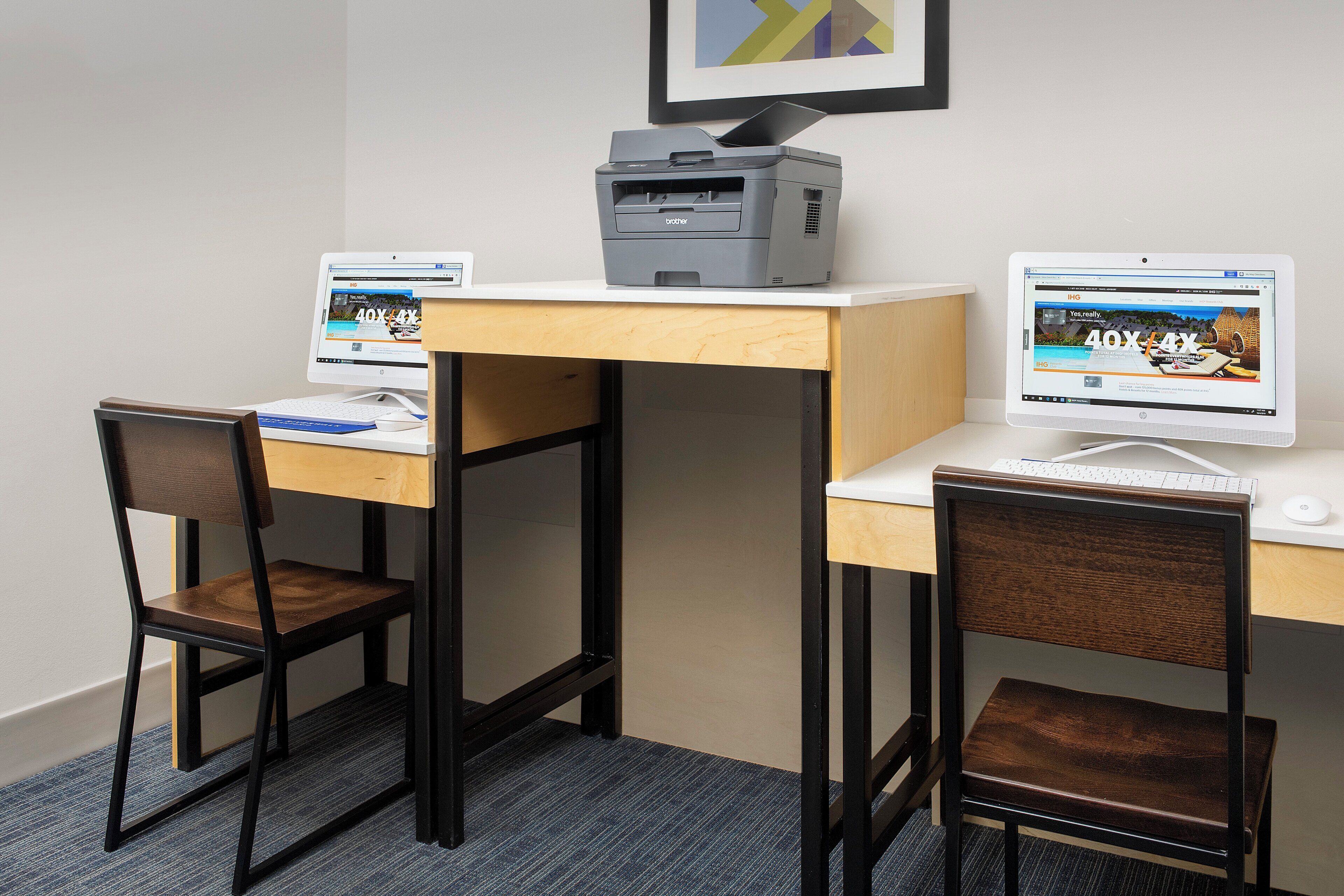 A workspace with two desks, each with a computer and a printer, and two chairs.