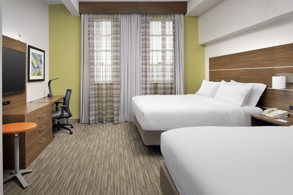 Una habitación de hotel con dos camas, un escritorio con silla, un televisor y una ventana con cortinas.