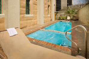 Un espace piscine comprenant deux bassins distincts, une chaise longue et une petite table avec une serviette.