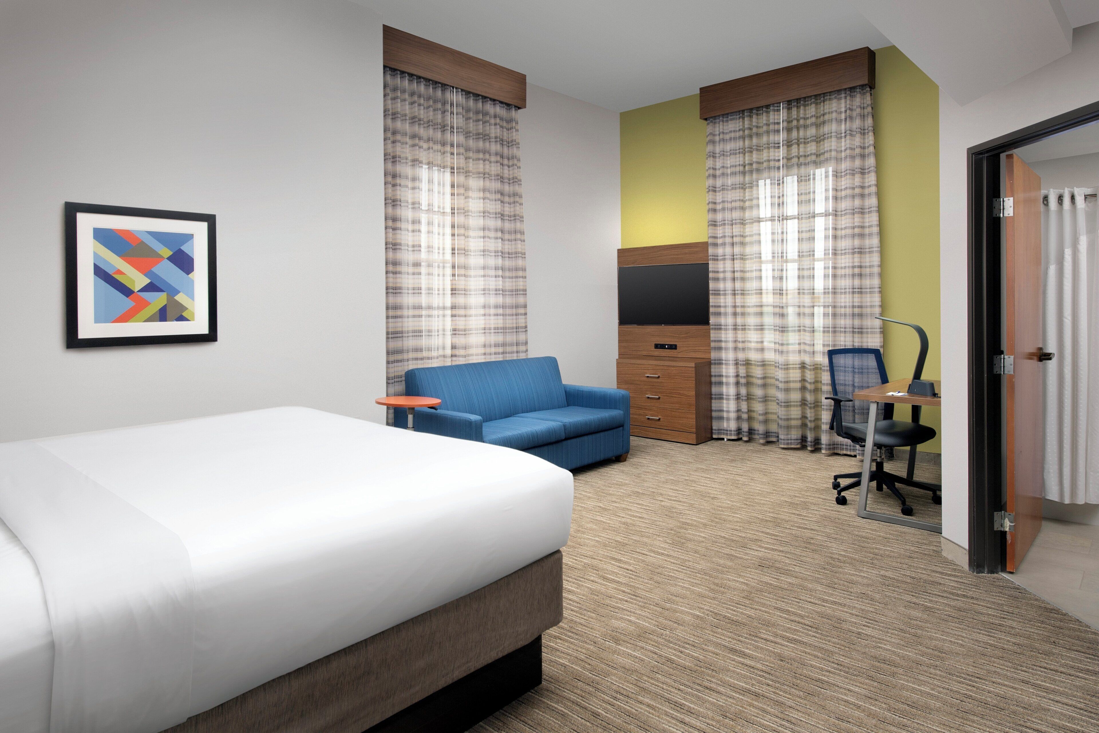 A hotel room with a bed, a blue sofa, a desk with a chair, and a television.