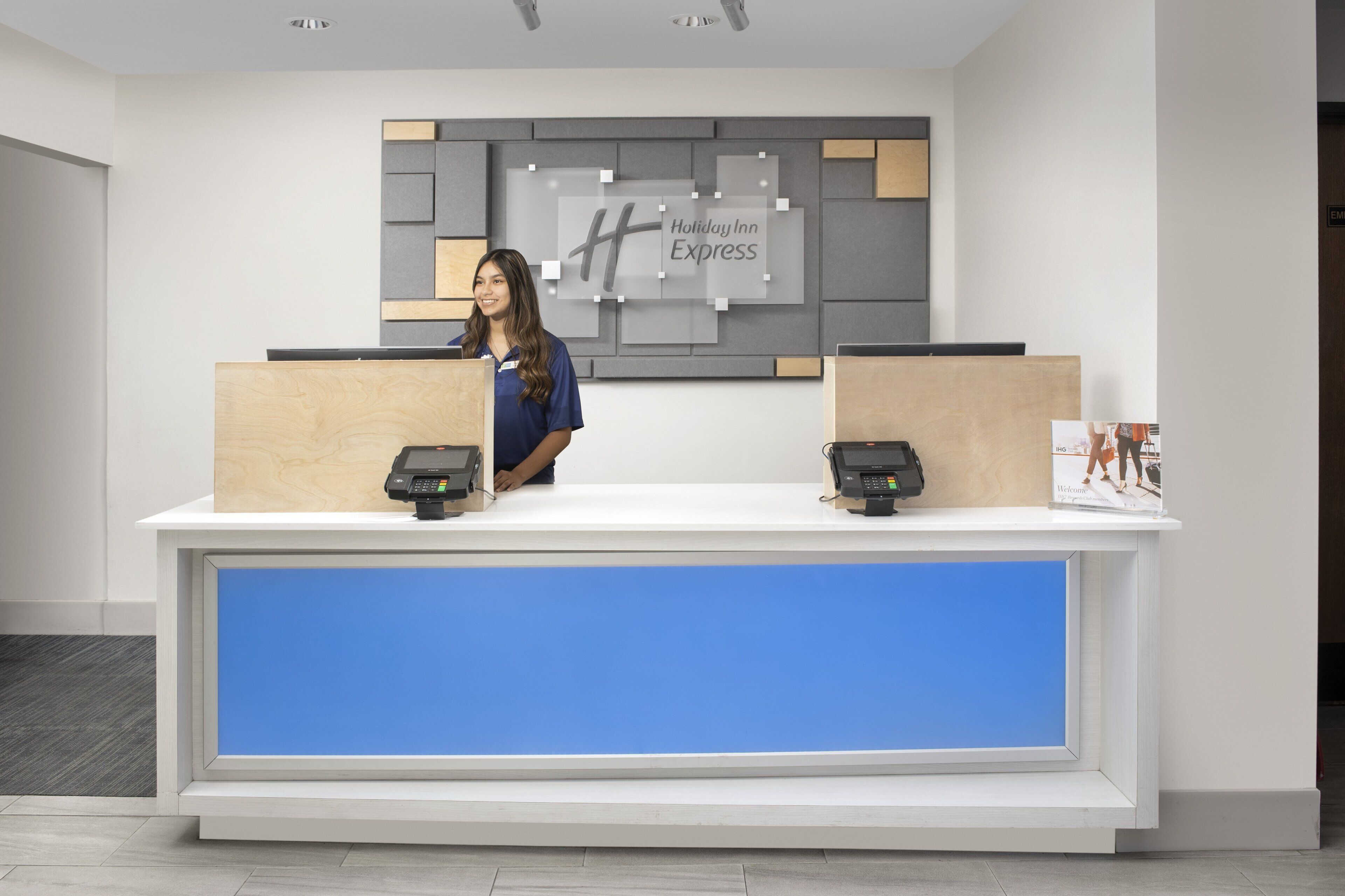 Un comptoir d’accueil d’hôtel au design moderne, deux réceptionnistes et une enseigne indiquant « Holiday Inn Express ».