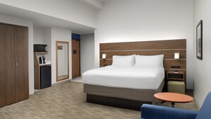 A hotel room with a large bed, a small table, a sofa, a wardrobe, a microwave, and a coffee machine.