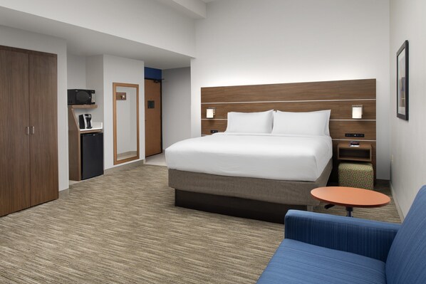 Habitación de hotel con una cama grande, una mesita pequeña, un sofá, un armario, un microondas y una cafetera.