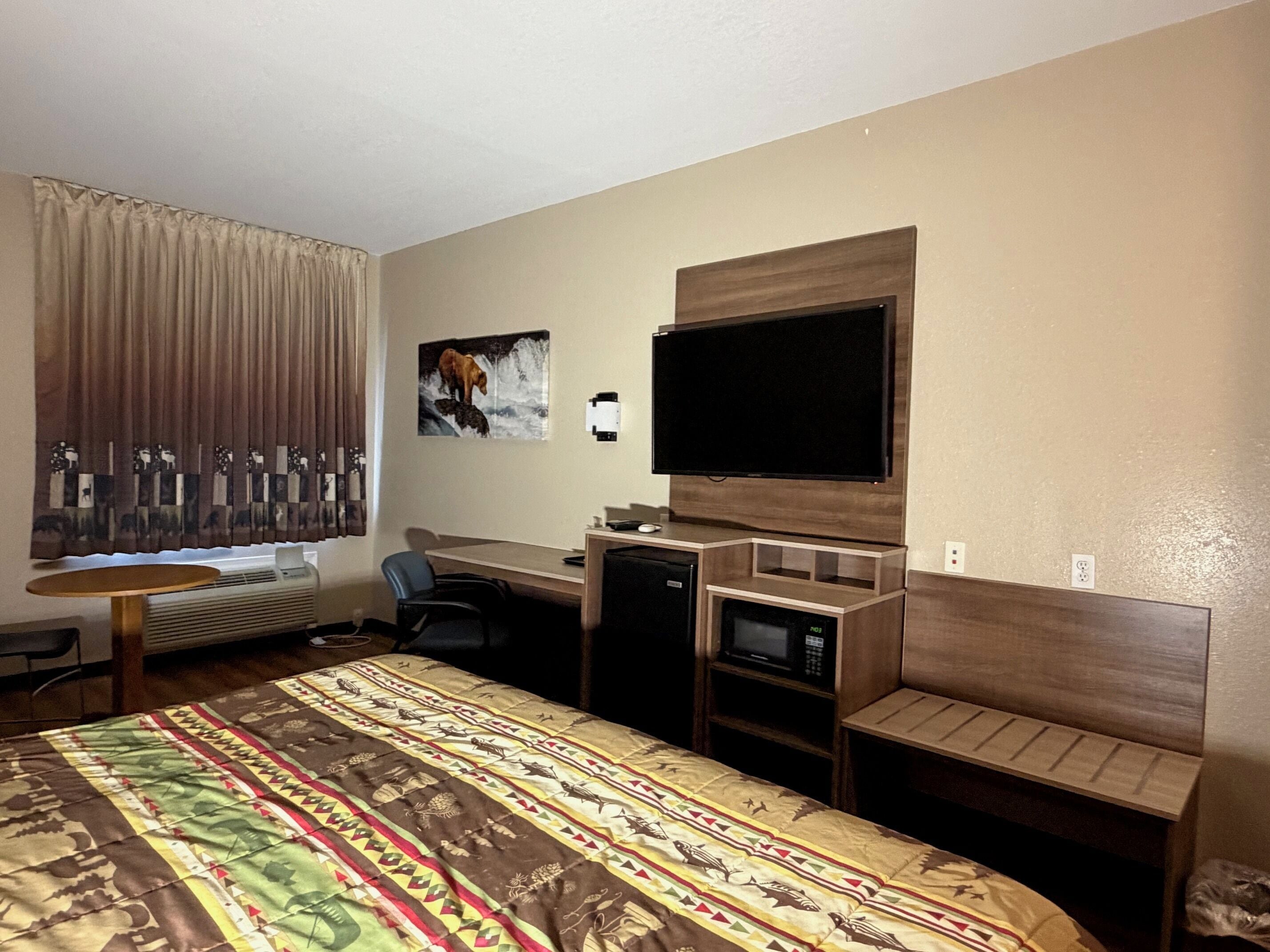Una habitación de hotel con una cama, un escritorio con computadora, un televisor y un microondas.