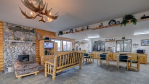 A log cabin interior with a stone fireplace, wooden furniture, a television, and a kitchen area. - Booneslick Lodge of Neosho (Neosho)