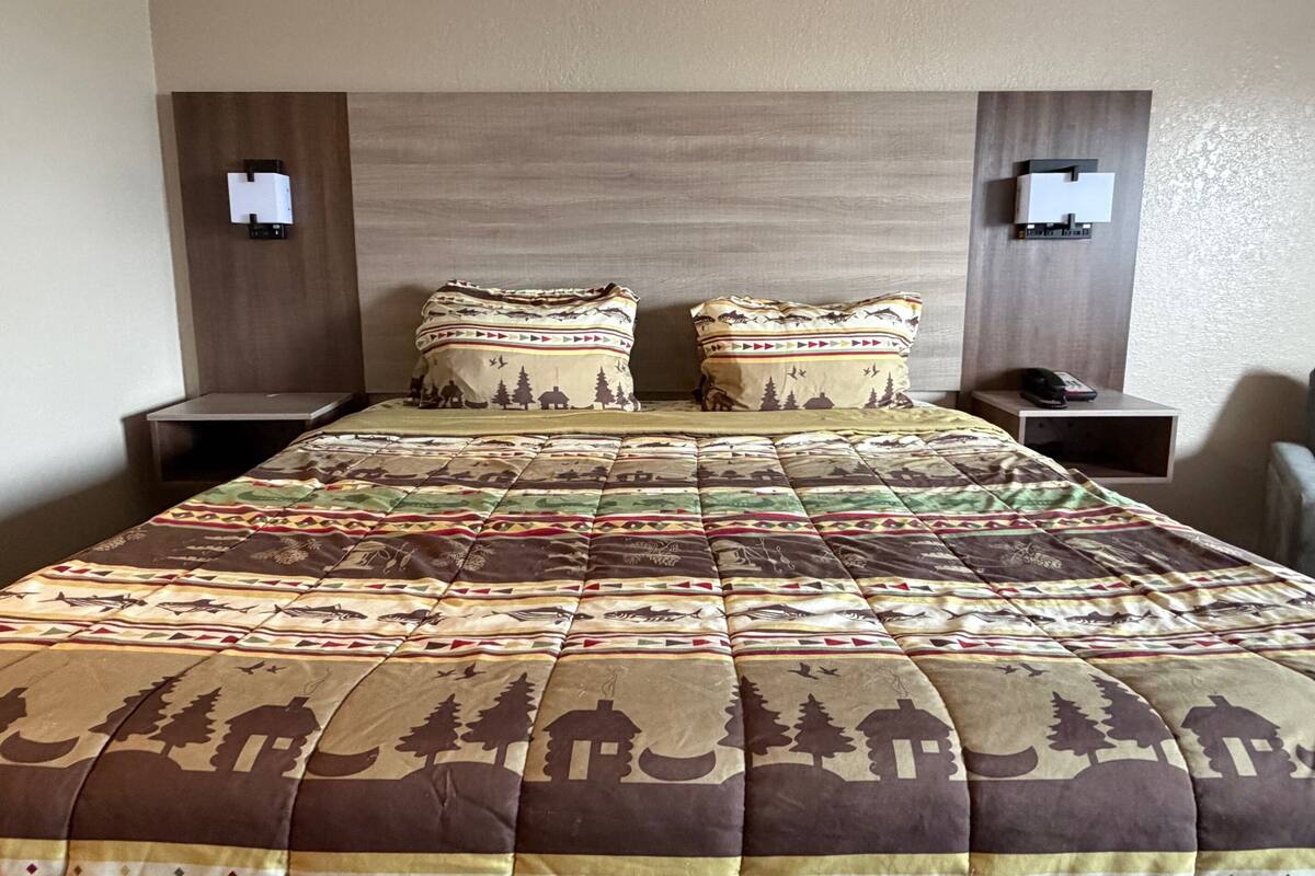 A hotel room with a large bed, two nightstands, and a headboard with wall-mounted lights.