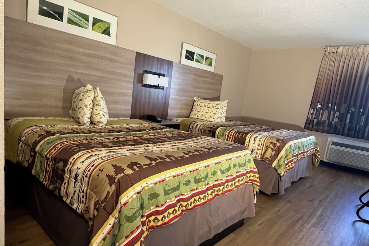A hotel room with two beds, each with patterned bedding, a wooden headboard, and a wall-mounted air conditioning unit.