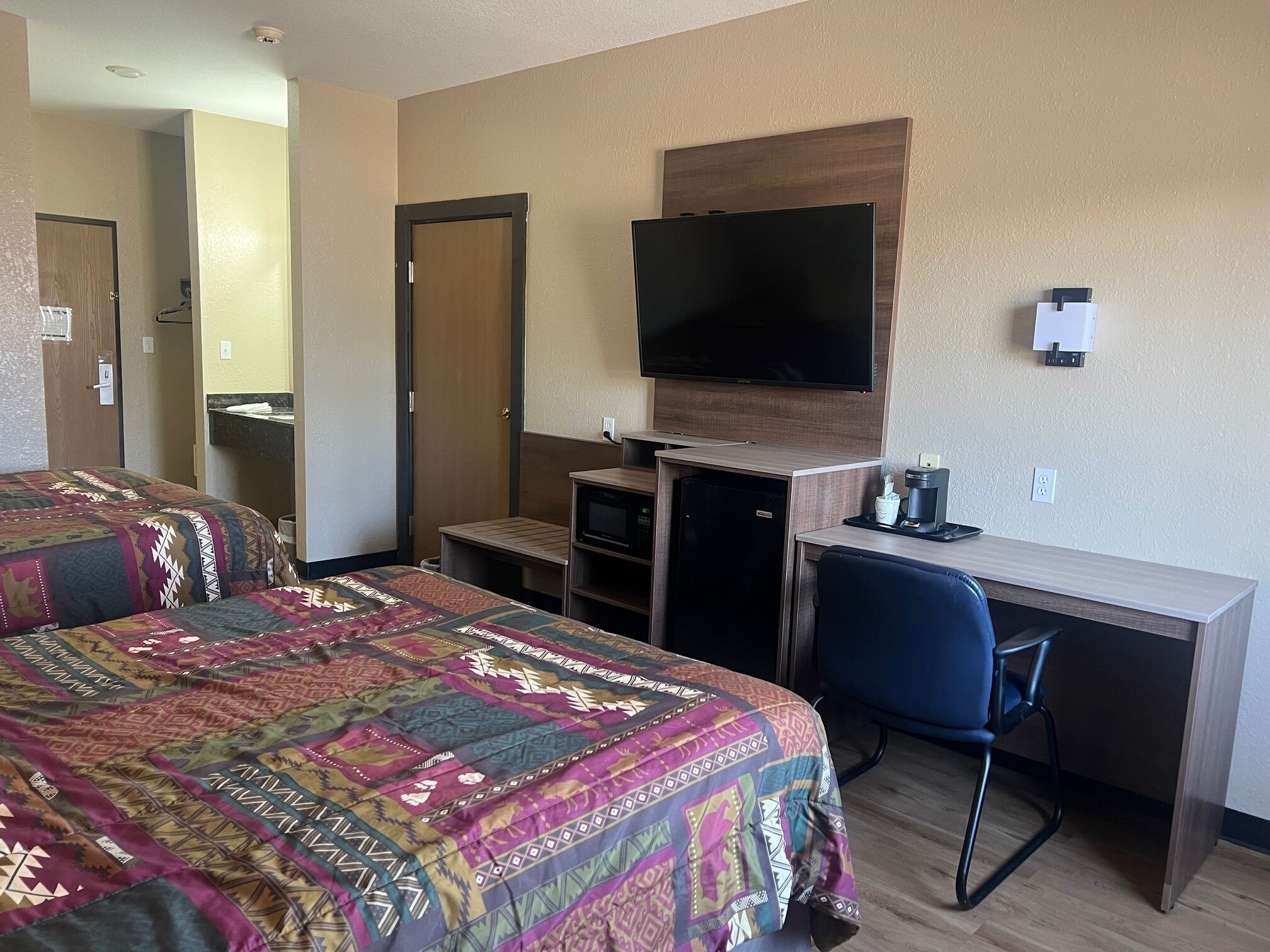 Ein Hotelzimmer mit zwei Betten, einem Schreibtisch, einem Fernseher, einer Kaffeemaschine und einem kleinen Kühlschrank.