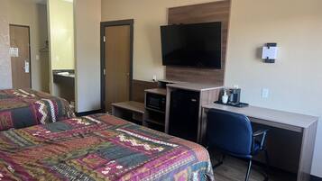 Ein Hotelzimmer mit zwei Betten, einem Schreibtisch, einem Fernseher, einer Kaffeemaschine und einem kleinen Kühlschrank.