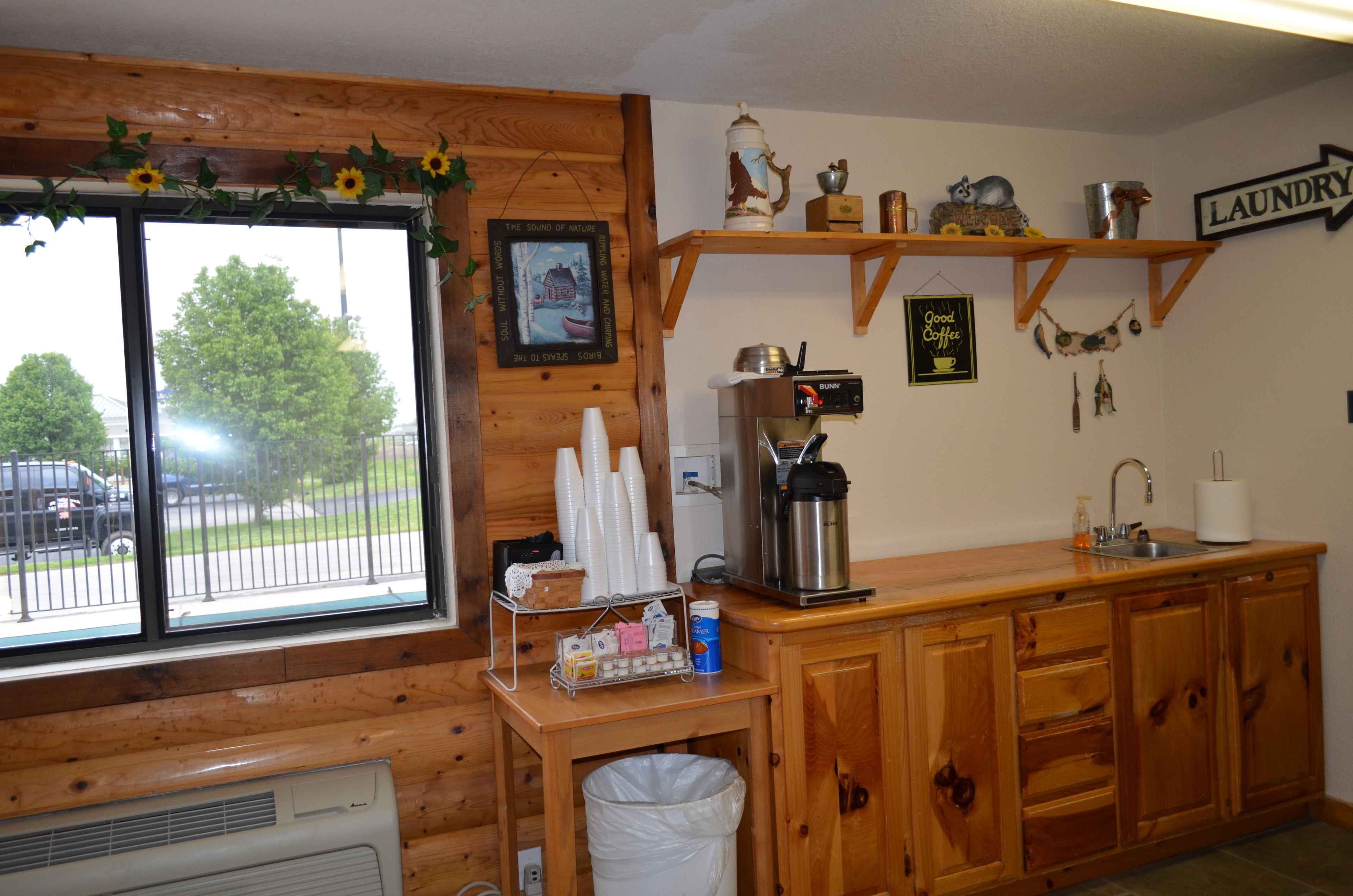 A kitchen with wooden cabinets, a coffee maker, and a window with a view of a street and trees.