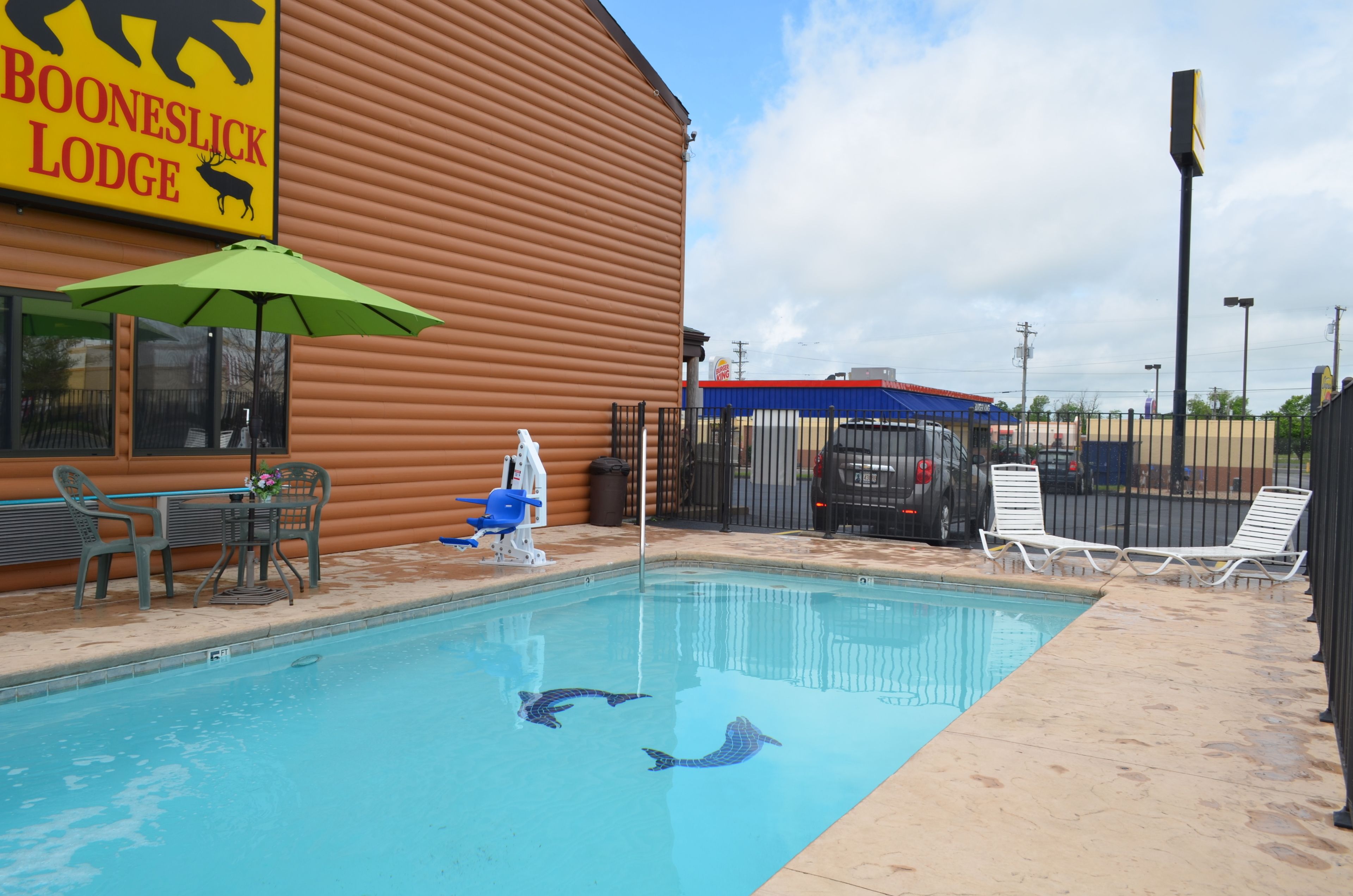 A pool area with lounge chairs, a table with chairs, and a sign for Booneslick Lodge.