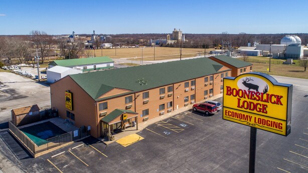 A large building with a green roof, a sign for Booneslick Lodge, and a parking lot with several cars. - Booneslick Lodge of Neosho (Neosho)