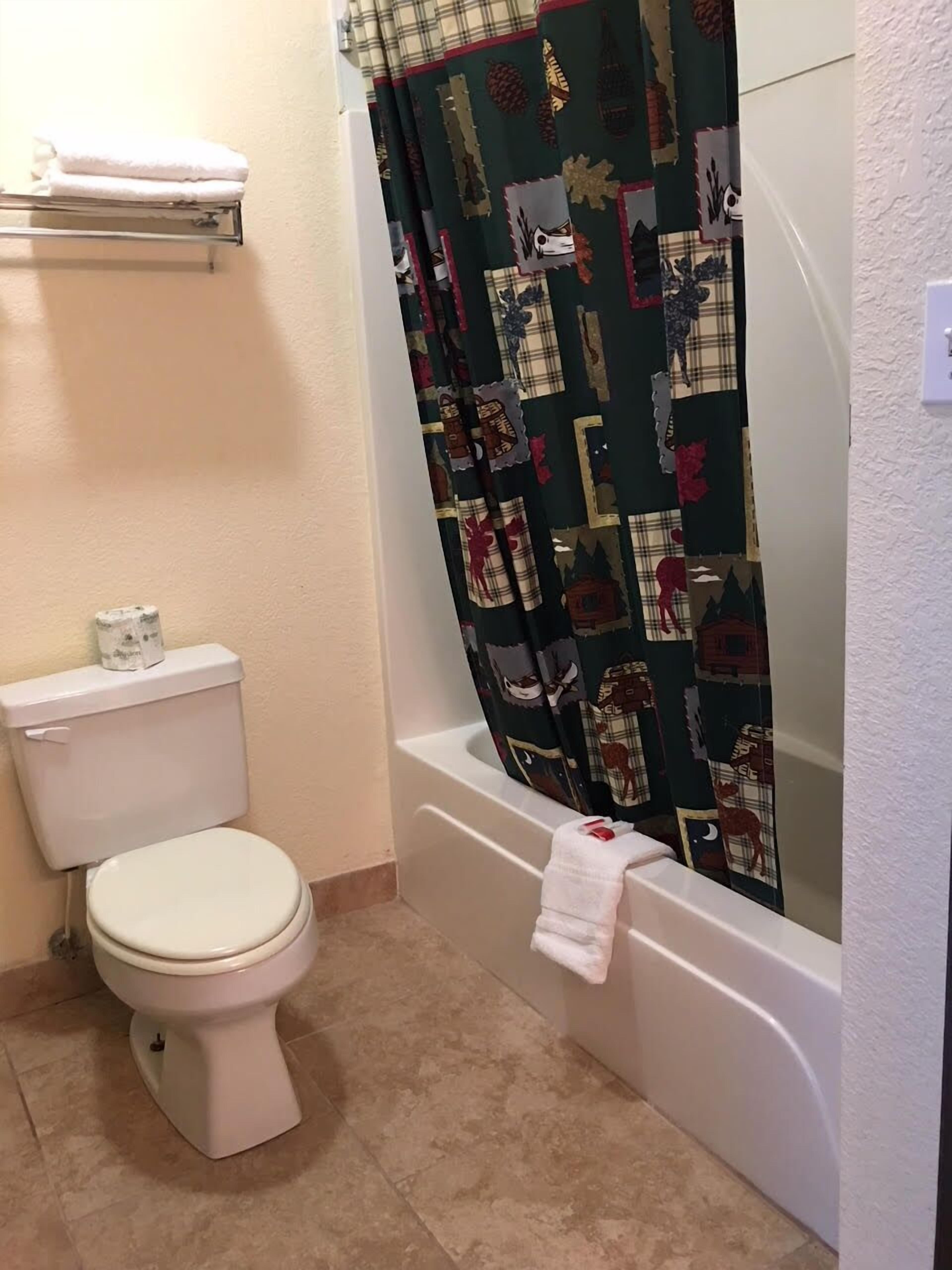 Une salle de bain équipée de toilettes, d’une baignoire et d’un rideau de douche à motifs écossais.