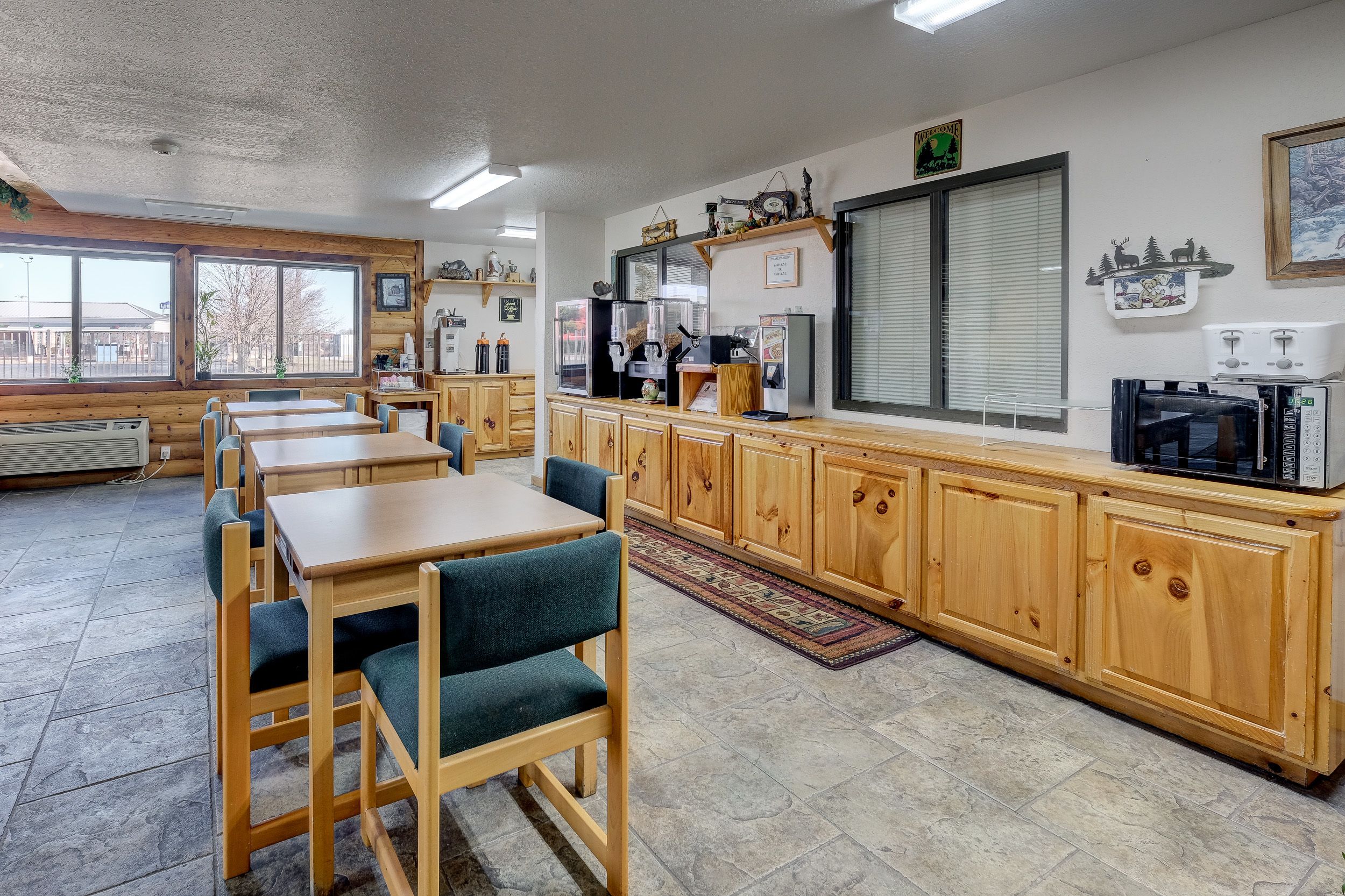 Un comedor con mesas y sillas de madera, una encimera de cocina con electrodomésticos y ventanas amplias.