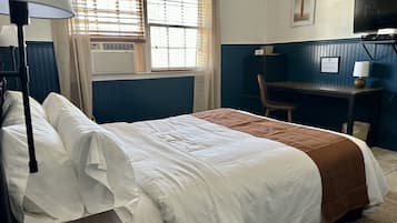 A hotel room with a bed, a desk, a chair, a television, and a window with blinds.