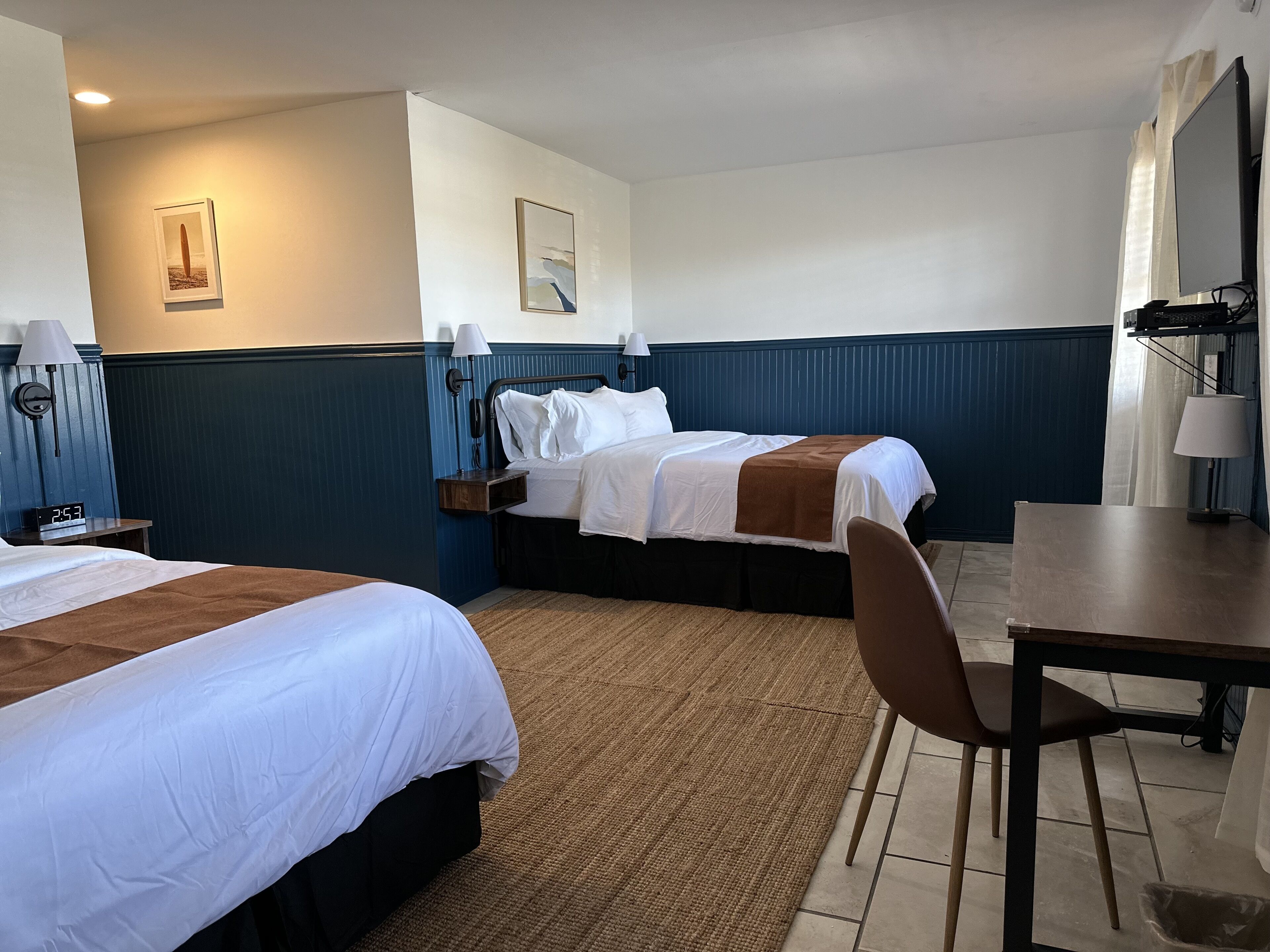 A hotel room with two beds, a desk, and a chair.
