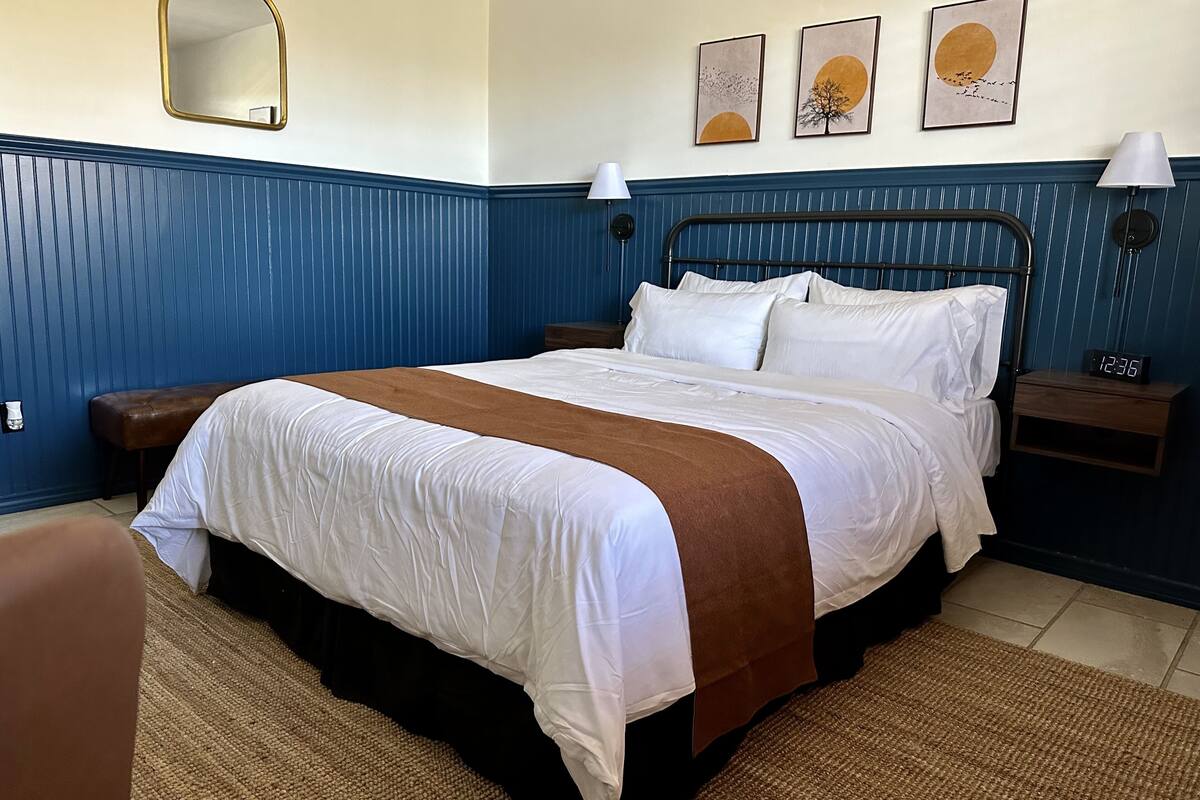 A neatly made bed with white and brown bedding, a bedside table with a lamp, and a wall clock.