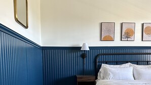 A bedroom with a bed, bench, lamp, and artwork on the wall.