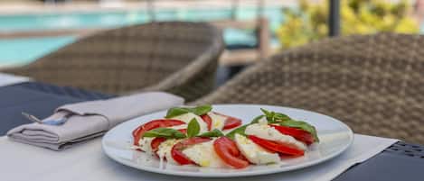 A plate of Caprese salad on a table by a poolside lounge area.