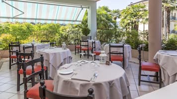 Un restaurante con mesas redondas, sillas rojas acolchadas y vistas a palmeras y edificios.