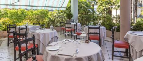 Un restaurant avec des tables rondes, des chaises rembourrées de couleur rouge et une vue sur les palmiers et les immeubles.