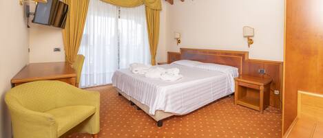 Quarto de hotel com cama, cadeira, televisão e teto de madeira.