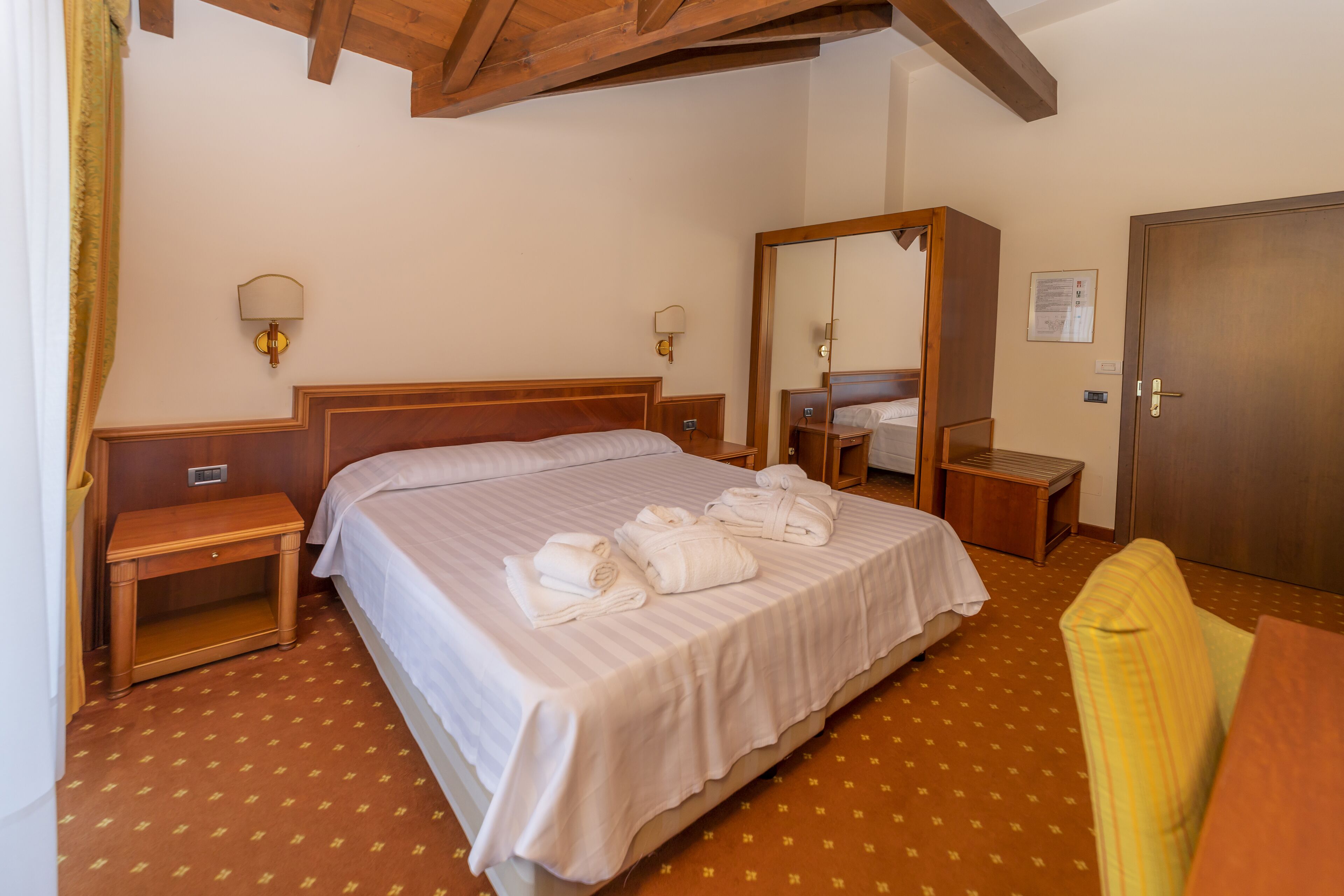 Una camera d'albergo con un letto grande, comodini, un armadio in legno e uno specchio.