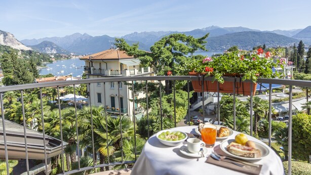 A balcony with a table set for breakfast, overlooking a lake and mountains. - Hotel Della Torre (Stresa)