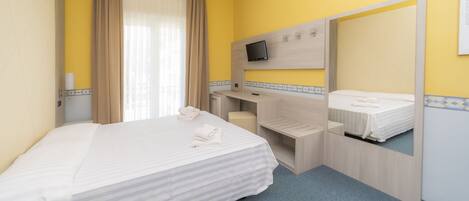 A hotel room with a bed, a desk, a chair, a TV, and a mirror.