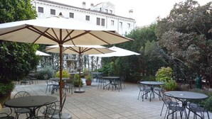 Un espace extérieur aménagé en terrasse, avec des tables et des chaises rondes, entouré de plantes en pot et d’arbres.