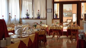 Une salle à manger avec des tables dressées, un lustre et une vue par les fenêtres.