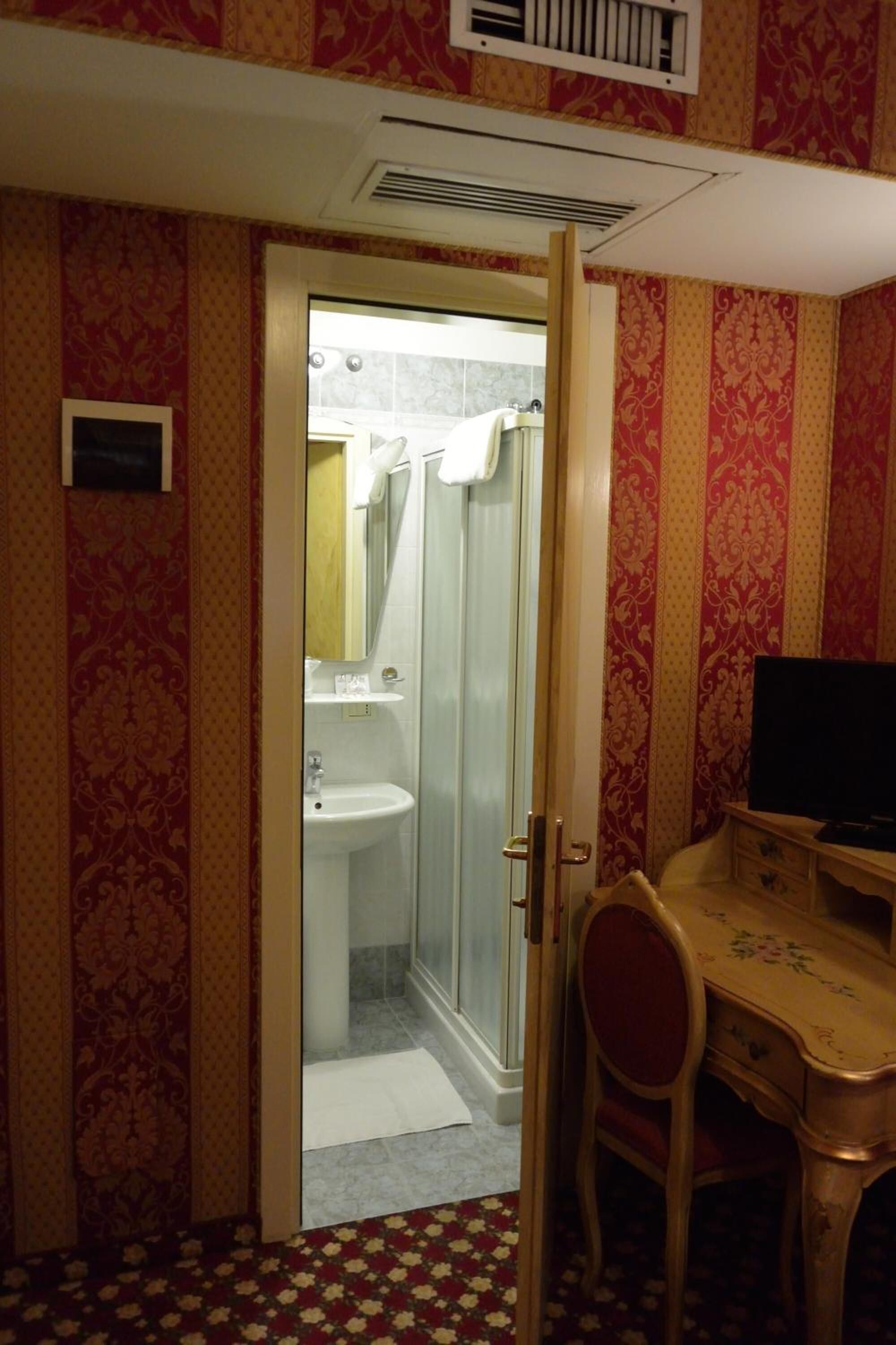 A bathroom with a shower, sink, and a desk with a chair.
