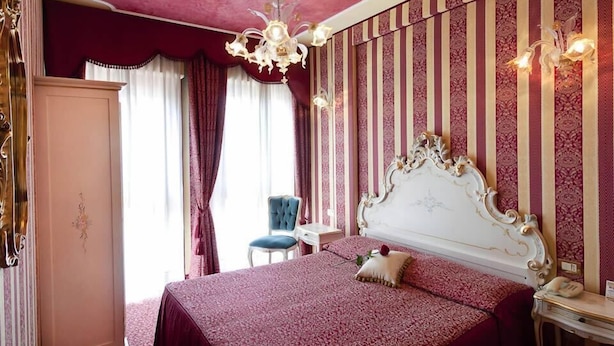 Une chambre à coucher avec un grand lit, un lustre, une coiffeuse avec un miroir et un papier peint à rayures.