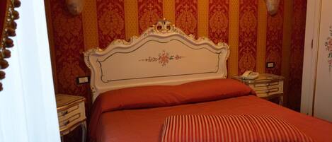 A bed with a white headboard and red bedding in a room with striped wallpaper.