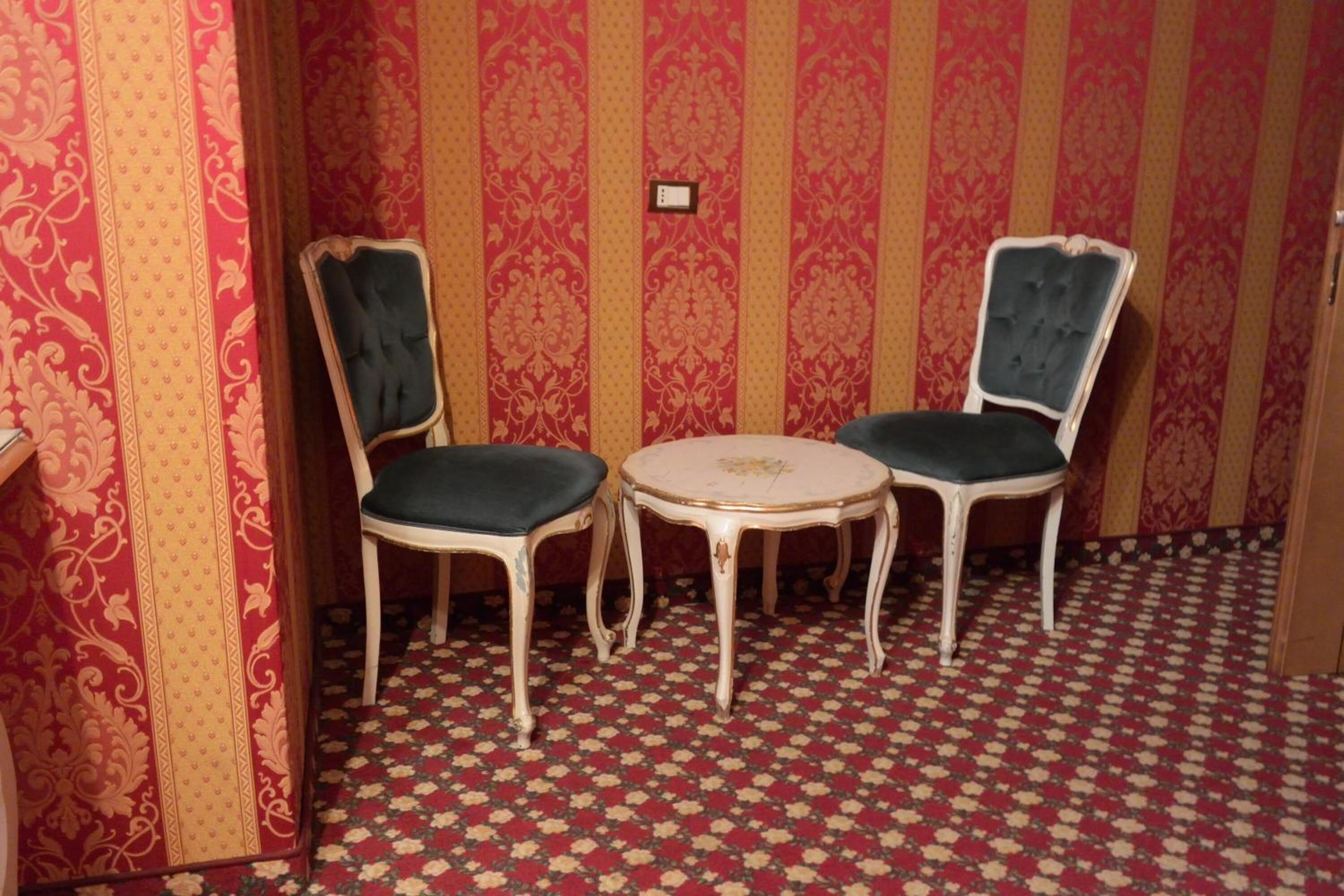 A room with two chairs and a small table, patterned wallpaper, and a patterned carpet.