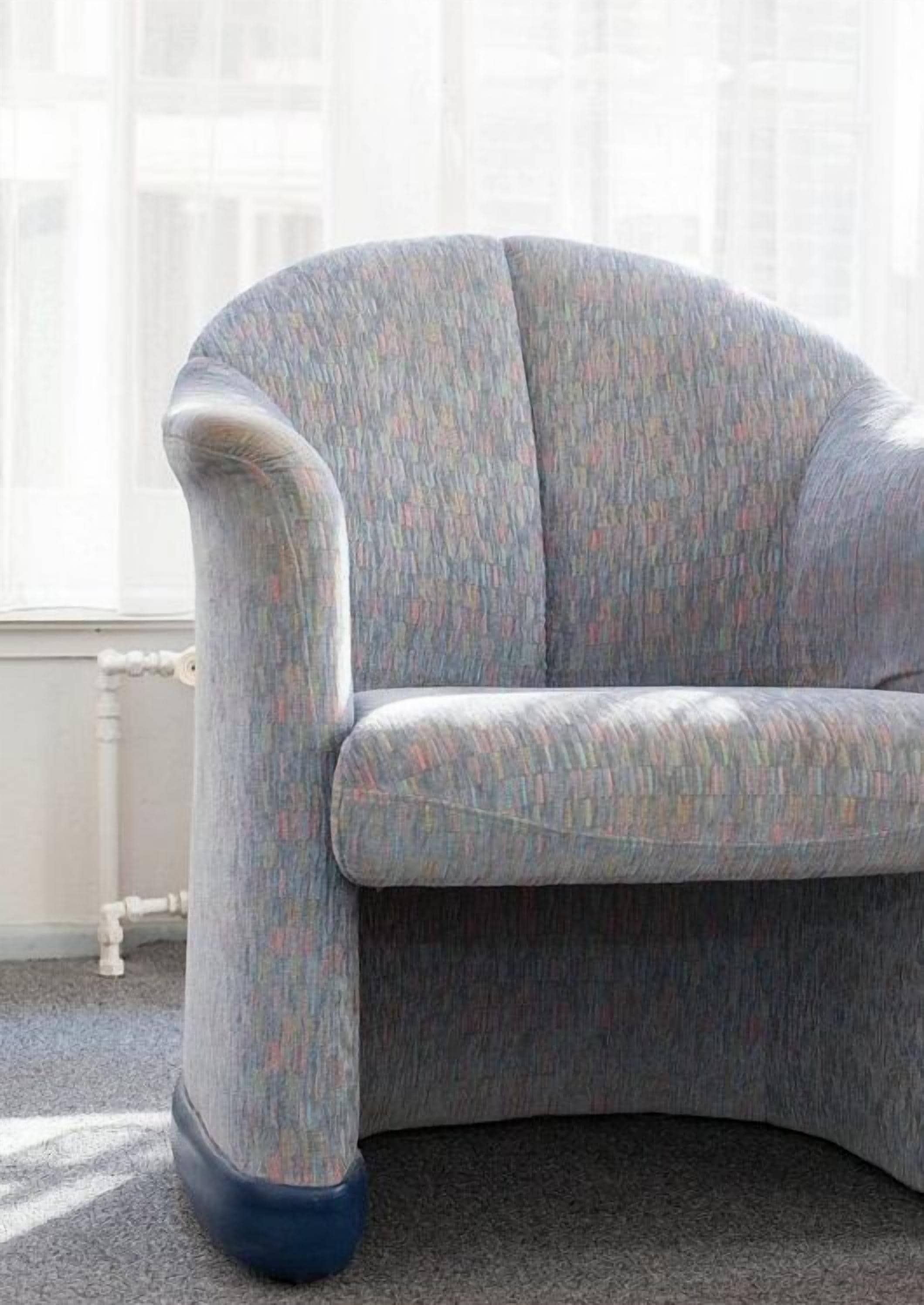 A corner sofa with a textured fabric, positioned in a room with a white radiator and a window with blinds.