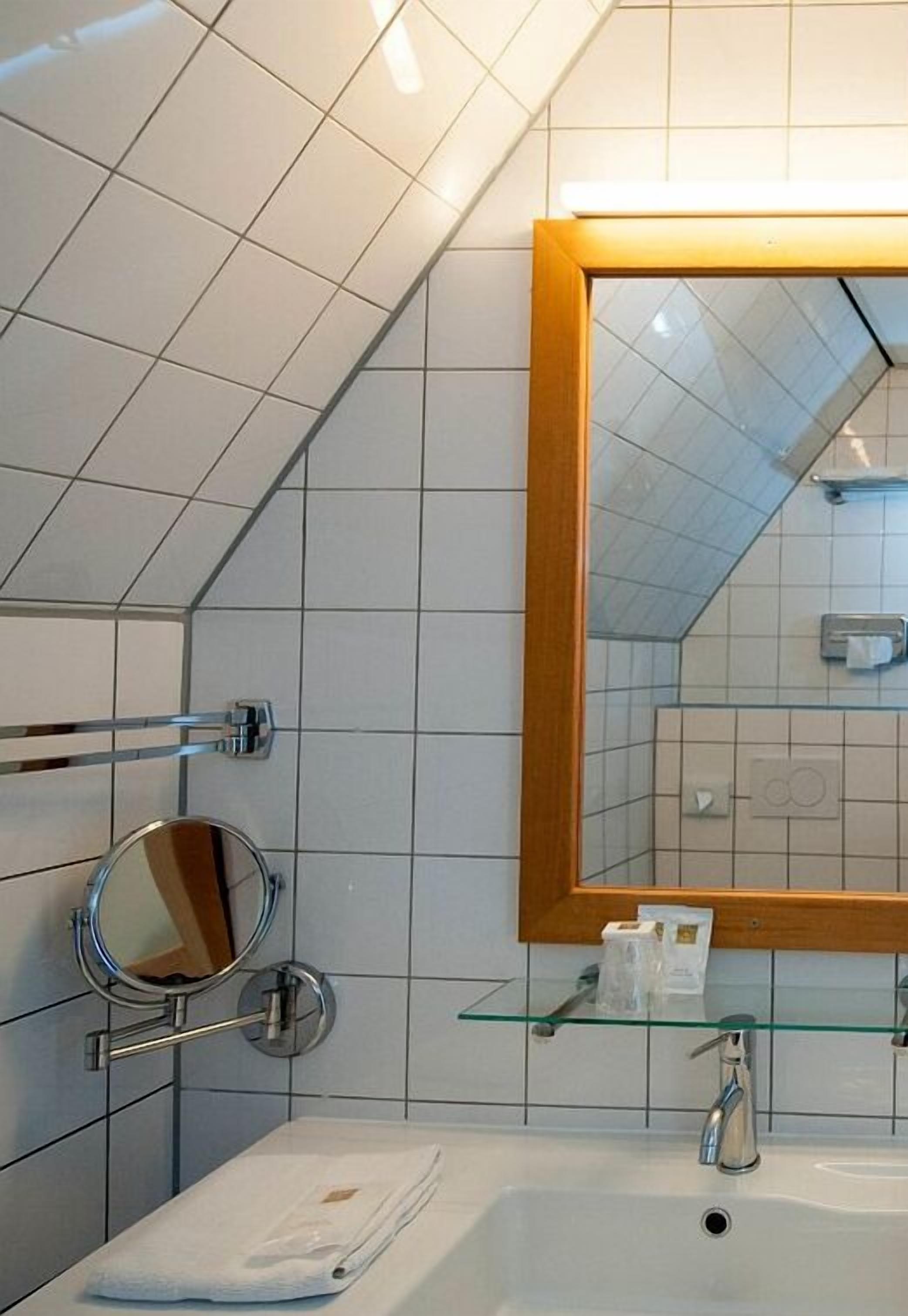 Ein modernes Badezimmer mit einem großen Spiegel, einem Waschbecken und einem Glastablett mit Pflegeprodukten.