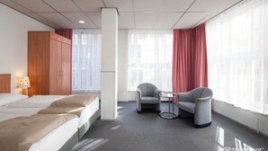 A hotel room with a bed, a chair, a small table, and a window with curtains. - Rho Hotel (Amsterdam)