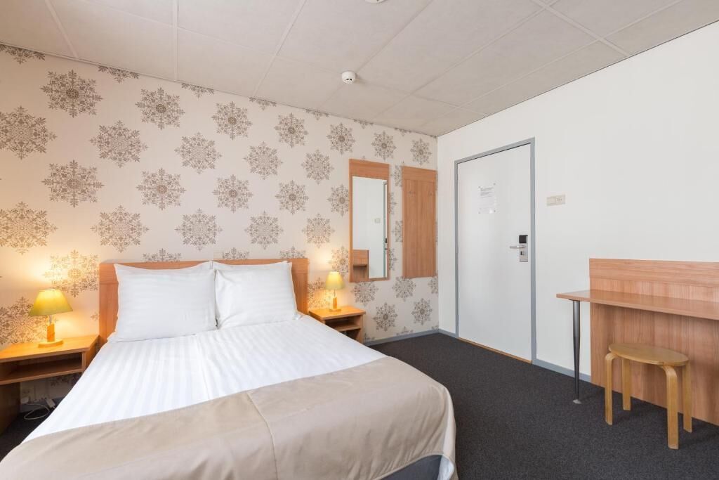 Ein Hotelzimmer mit einem Bett, zwei Nachttischlampen, einem Holztisch, einem Stuhl, einem Spiegel und einer Tür.