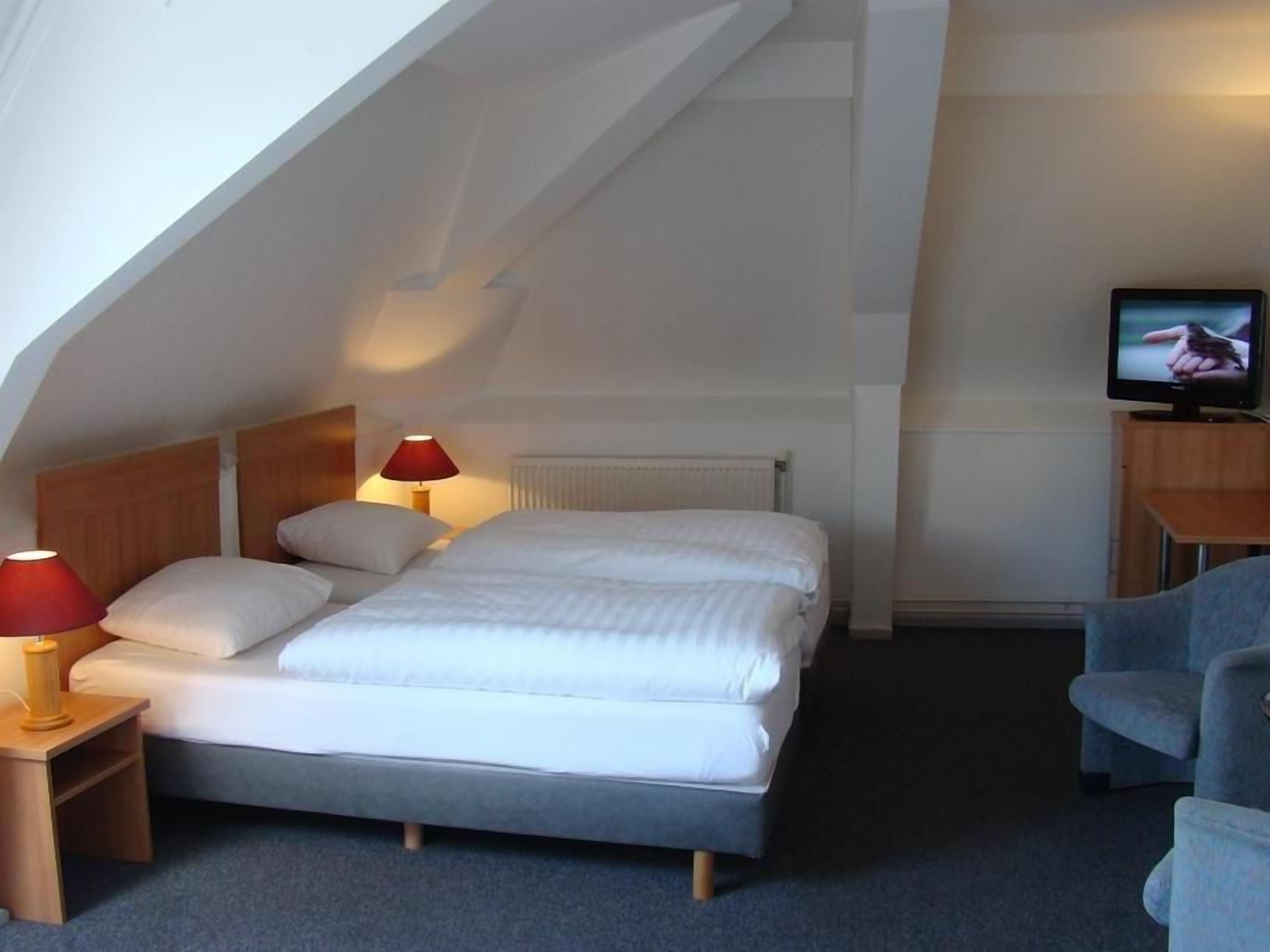A bedroom with a bed, two bedside lamps, a television, and a chair.